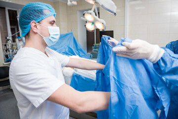 Assistant helps the surgeon put on latex gloves and surgical gown before the operation.