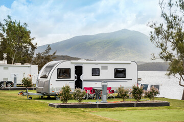 RV caravan camping at the caravan park on the lake with mountains on the horizon. Camping vacation travel concept - obrazy, fototapety, plakaty