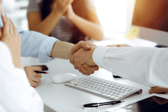 Two businessmen shaking hands in sunny office, close-up. Colleagues applauding of success meeting end