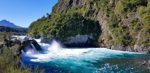 Cascada de río en aguas azules con volcán a fondo, rodeando de montaña 