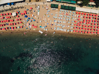 Many bright sun umbrellas stand on the beach in Budva near the blue sea