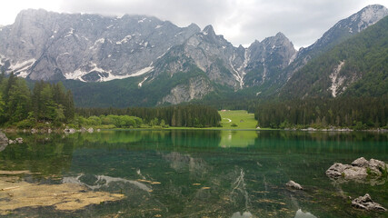 Tarvisio, Italy - May 29, 2020: A static shot from the shore of Fusine lake in the Julian Alps with snowy mountains in background. Beautiful nature in a spring cloudy day, no people around