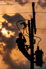 The silhouette of power lineman climbing on an electric pole with a transformer installed. And...