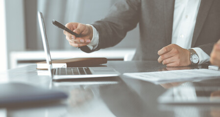 Unknown businessmen and woman sitting, using laptop computer and discussing questions at meeting in modern office, close-up