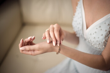 Obraz na płótnie Canvas A beautiful young bride in a white long dress touches a gold bracelet on her arm with her hand. Blue, yellow, white, gold, beige.