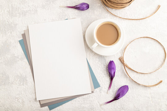 White paper sheet mockup with spring snowdrop crocus flowers and cup of coffee on gray concrete background. top view, copy space.