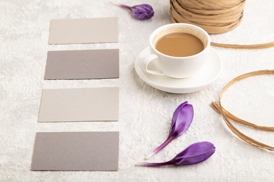 Gray paper business card mockup with spring snowdrop crocus flowers and cup of coffee on gray concrete background. side view, copy space.