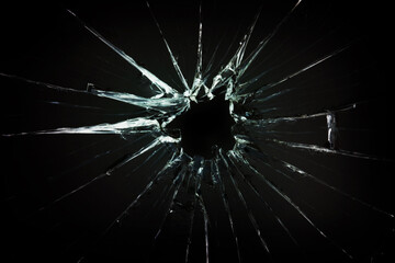 The hole in the broken and cracked glass, closeup on dark background - obrazy, fototapety, plakaty