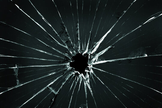 The hole in the broken and cracked glass, closeup on dark background