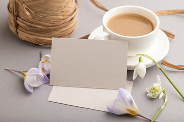Gray paper business card mockup with spring snowdrop crocus and galanthus flowers and cup of coffee on gray background. side view, copy space.