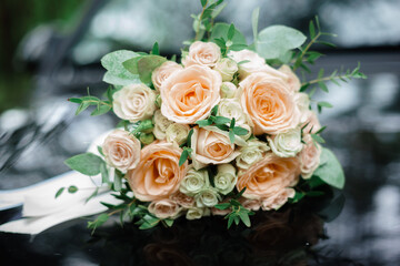 A gorgeous bouquet of large white and beige, pink roses lies on the glossy hood of a black car and is reflected.