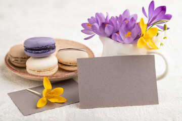 Gray paper business card mockup with spring snowdrop crocus flowers and multicolored macaroons on gray concrete background. side view, copy space.