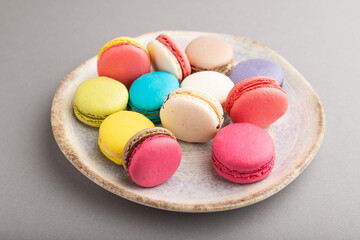 Different colors macaroons on ceramic plate on gray pastel background. side view, close up.