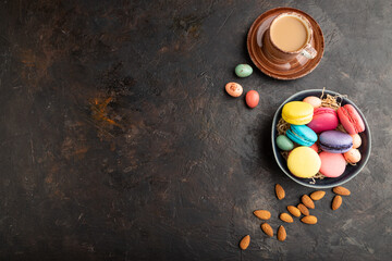 Obraz na płótnie Canvas Different colors macaroons and chocolate eggs in ceramic bowl, cup of coffee on black concrete background. top view, copy space.