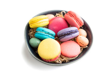 Different colors macaroons and chocolate eggs in blue ceramic bowl isolated on white background. side view, close up.