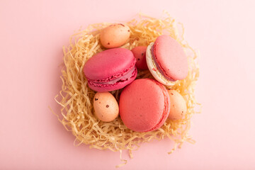 Magenta and pink macaroons and chocolate eggs in decorative paper nest on pink pastel background. top view, close up.