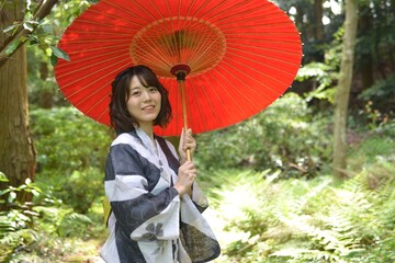 新緑に囲まれて和傘を手に持つ浴衣女性