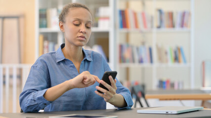 Serious African Woman using Smartphone in Library