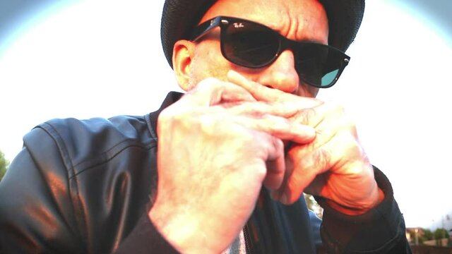 Man with hat plays blues with harp- slow motion- rack focus
