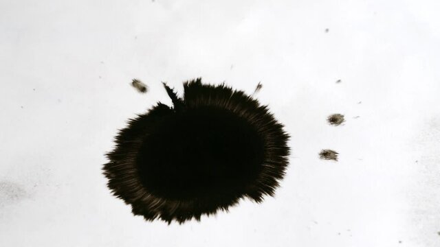 The ink drips on a white paper and spread rapidly, forming an irregular circle.