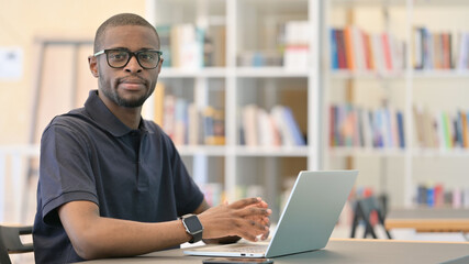 Young African Man with Laptop Looking at Camera in Library