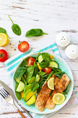 Grilled salmon fillet close-up with spinach, cucumber, tomato and avocado salad on a white wooden table. Top view, flat lay. Copy space.