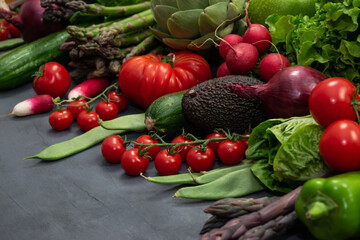 Different organic vegetables - asparagus, tomatoes cherry, avocado, artichoke, pepper, lime, redish, cauliflowerm, green beans, cucumber on gray background.