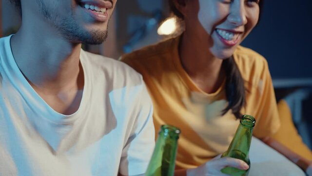 Happy young asian couple looking at camera enjoy night party event online sit couch video call with friends toast drink beer via video call online in living room at home, Social distancing concept.