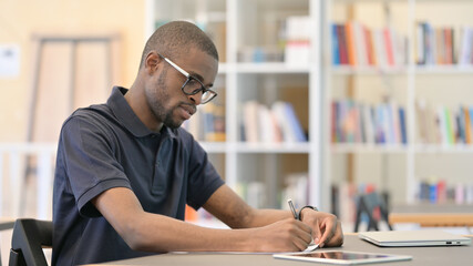 Young African Man Thinking and doing Paperwork in Library