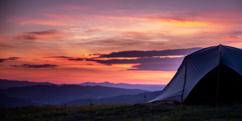 Tourist tent in the mountains under dramatic evening sky. Colorfull sunset in mountains. Camping travell concept. Traveler people enjoying the advanture alternative vacation © Zedspider