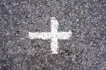 Old asphalt on the road. Cross drawn by paint and stains of oil. City environment. Top view close up.