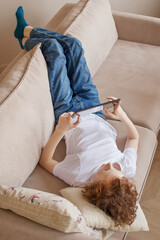 A teenager at home plays on a tablet, lies on a sofa.  Vertical photo.