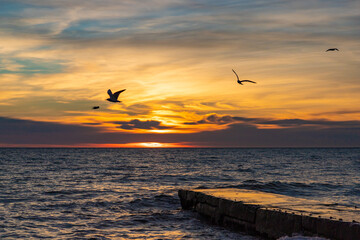 Beautiful sunset over the sea and stone pier with clouds and horizon on the beach in Sochi, Russia