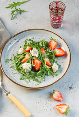 delicious salad with arugula, strawberries, ricotta and chia seeds. Overhead, on a gray background, vertical frame