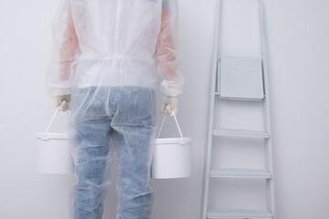 a man in protective clothing, bringing buckets of paint, against the background of a white wall and a stepladder, rear view