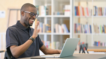 Cheerful Young African Man doing Video Chat on Laptop in Library