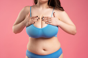 Woman checking her very large breasts for cancer on pink background