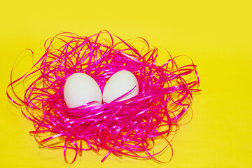 White eggs on pink hay over yellow color, bright easter background. Organic eggs.