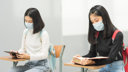 Female teenager college students wearing a face mask and keep distance while studying in classroom and college campus to prevent COVID-19 pandemic. Education stock photo