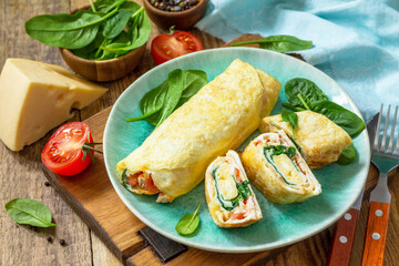 Japanese cuisine. National Japanese dish Omelet tamago yaki for breakfast. Rolled egg with spinach, tomato and cheese on a wooden table.