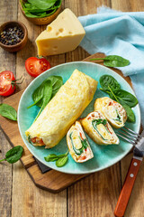 Japanese cuisine. National Japanese dish Omelet tamago yaki for breakfast. Rolled egg with spinach, tomato and cheese on a wooden table. Copy space.