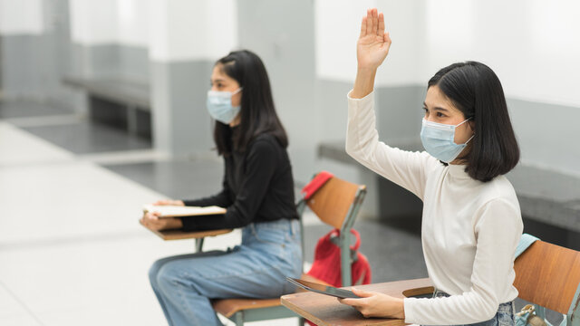 Female teenager college students wearing a face mask and keep distance while studying in classroom and college campus to prevent COVID-19 pandemic. Education stock photo - Powered by Adobe
