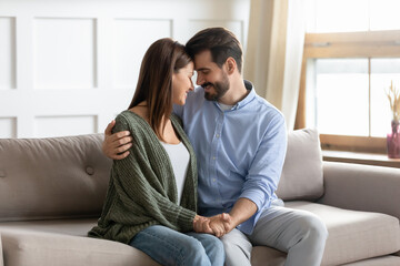 Naklejka na ściany i meble Happy young couple sit relax on sofa at home hug and cuddle show love and care in relationships. Smiling millennial Caucasian man and woman rest on couch enjoy romantic close date. Family concept.