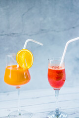 Freshly squeezed strawberry and orange juice in a glass on a blue and summer background. Fruit cocktails with plastic tubes on the table. Empty space for text