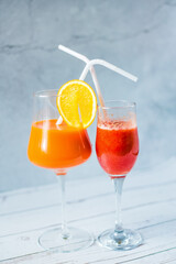 Freshly squeezed strawberry and orange juice in a glass on a blue and summer background. Fruit cocktails with plastic tubes on the table. Empty space for text