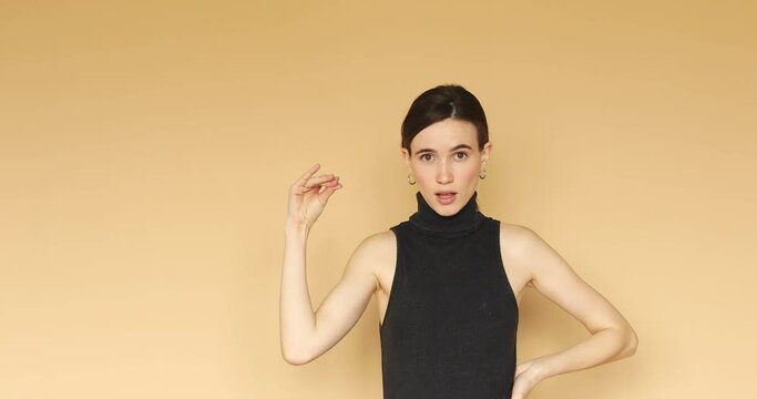 Bored brunette girl showing bla bla bla gesture, has not interested conversation isolated on beige background. Mocking expression.