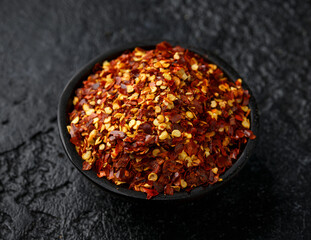 Dry chilli flake in wooden bowl on rustic dark background