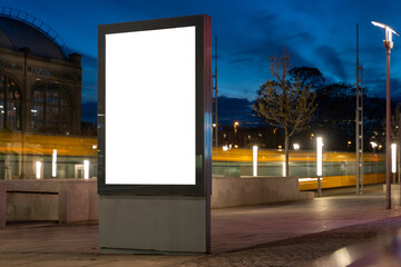 Advertisement billboard panel for a mockup. Empty template for ads in a city in the evening. Public transport moving in the background. Space for a commercial poster in the inner city. White display.