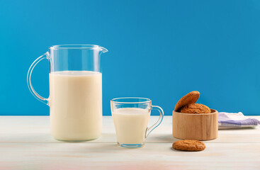 A jug and a glass of milk with cookies on a wooden table, on a blue background.Copy space.