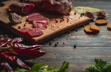 Sliced jerky. Sausage stick sliced on the board. Garlic red peppers and green parsley near the cold...